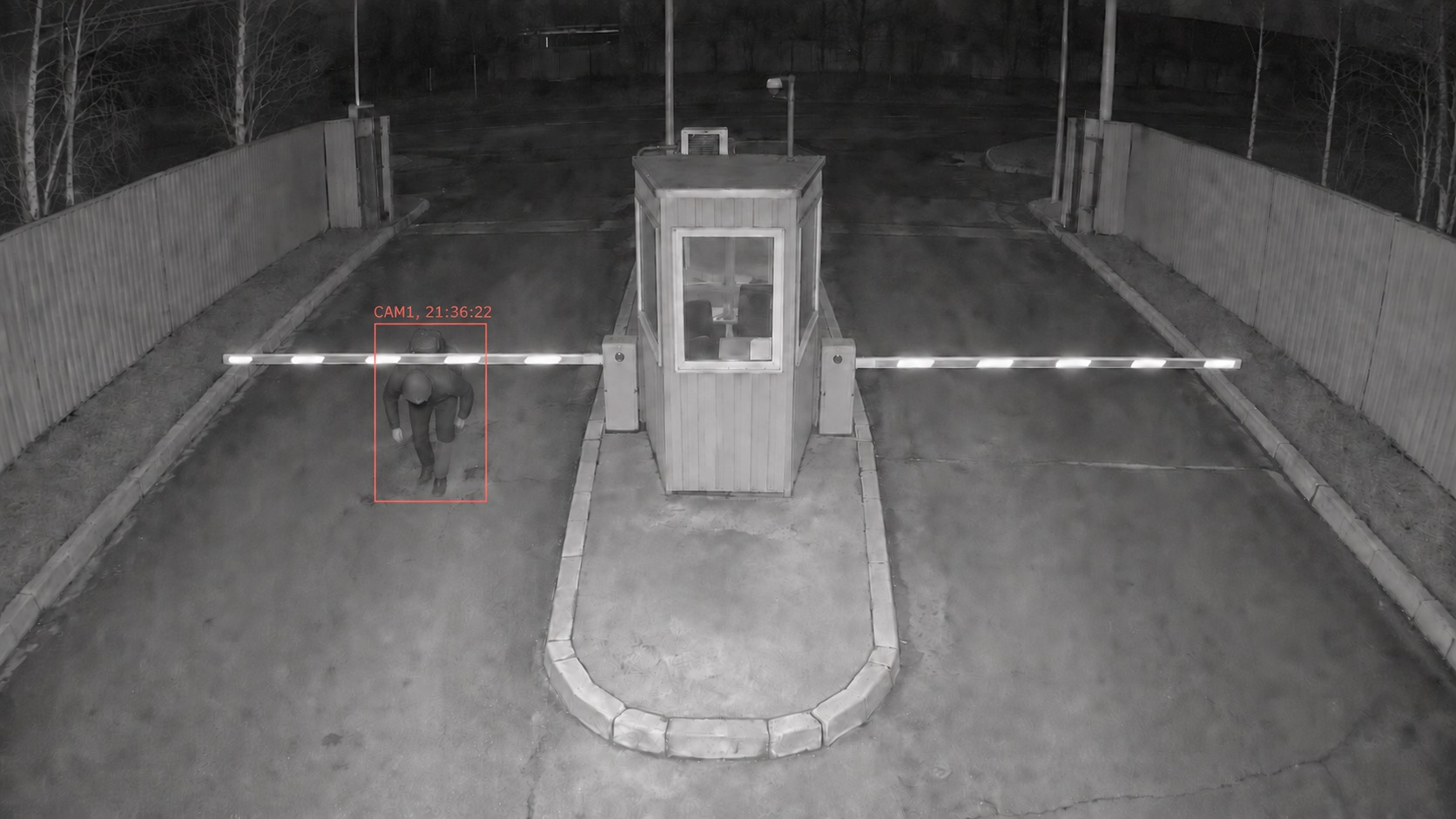 Человек проходит под шлагбаумом на охраняемую территорию.